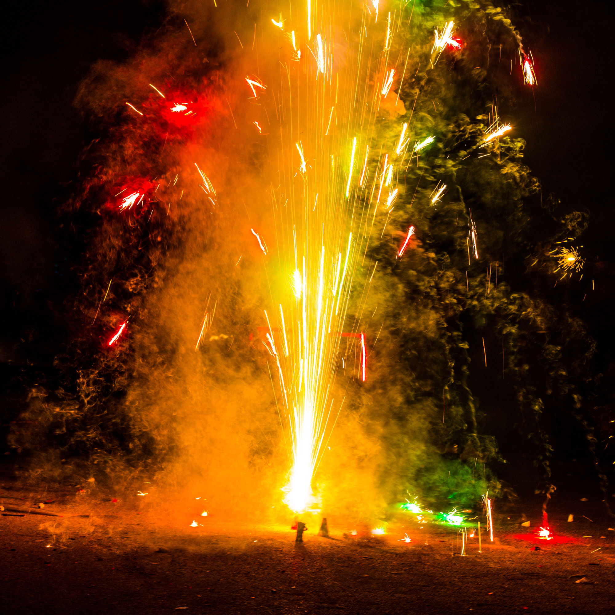 Photo of firecracker erupting in yellow, red, and green sparks.