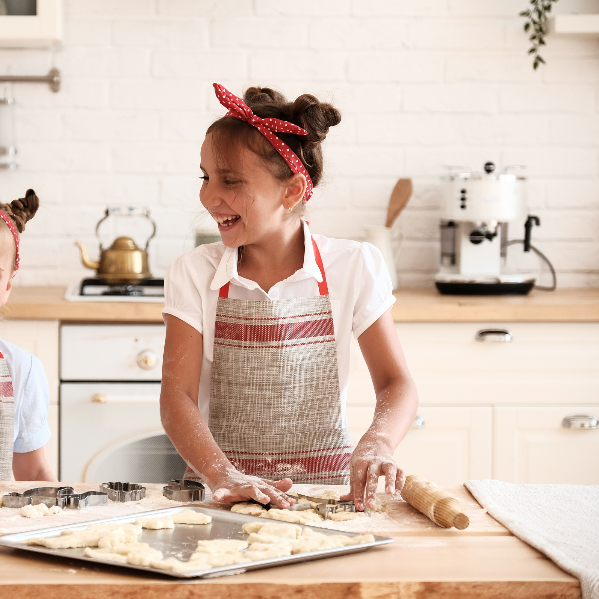 Photo of female child using cookie cutters to cut out cookie dough.