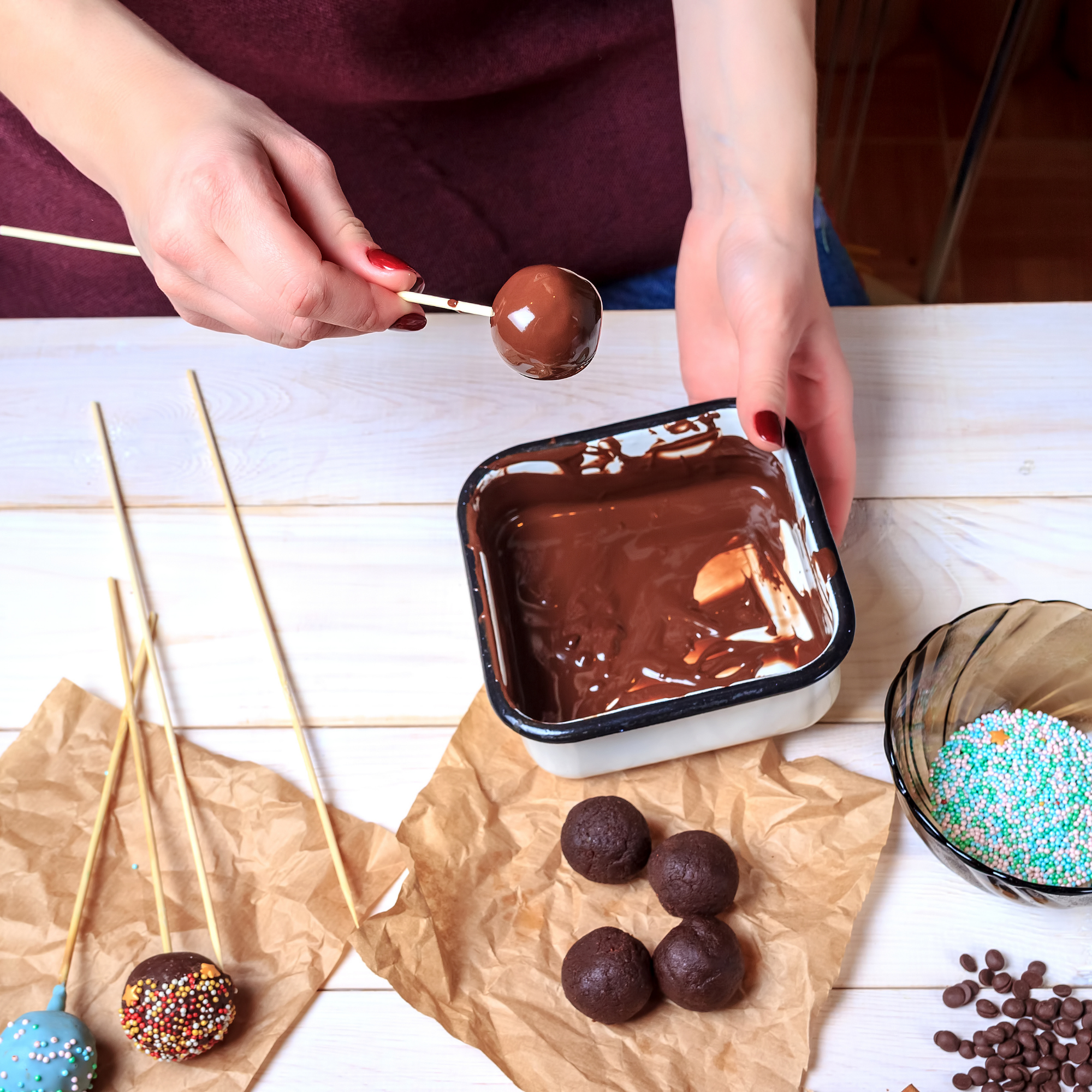 Photo shows someone's hands dipping chocolate cake pops into melted chocolate.