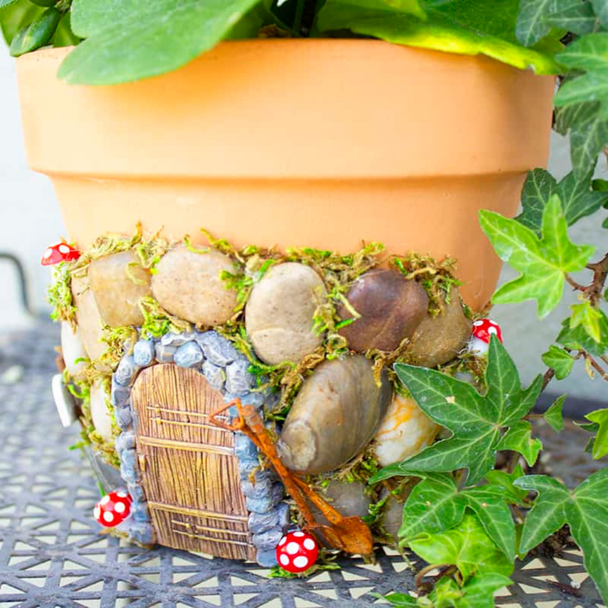 Rocks, greenery and a door placed on a clay flowerpot to create a fairy house.