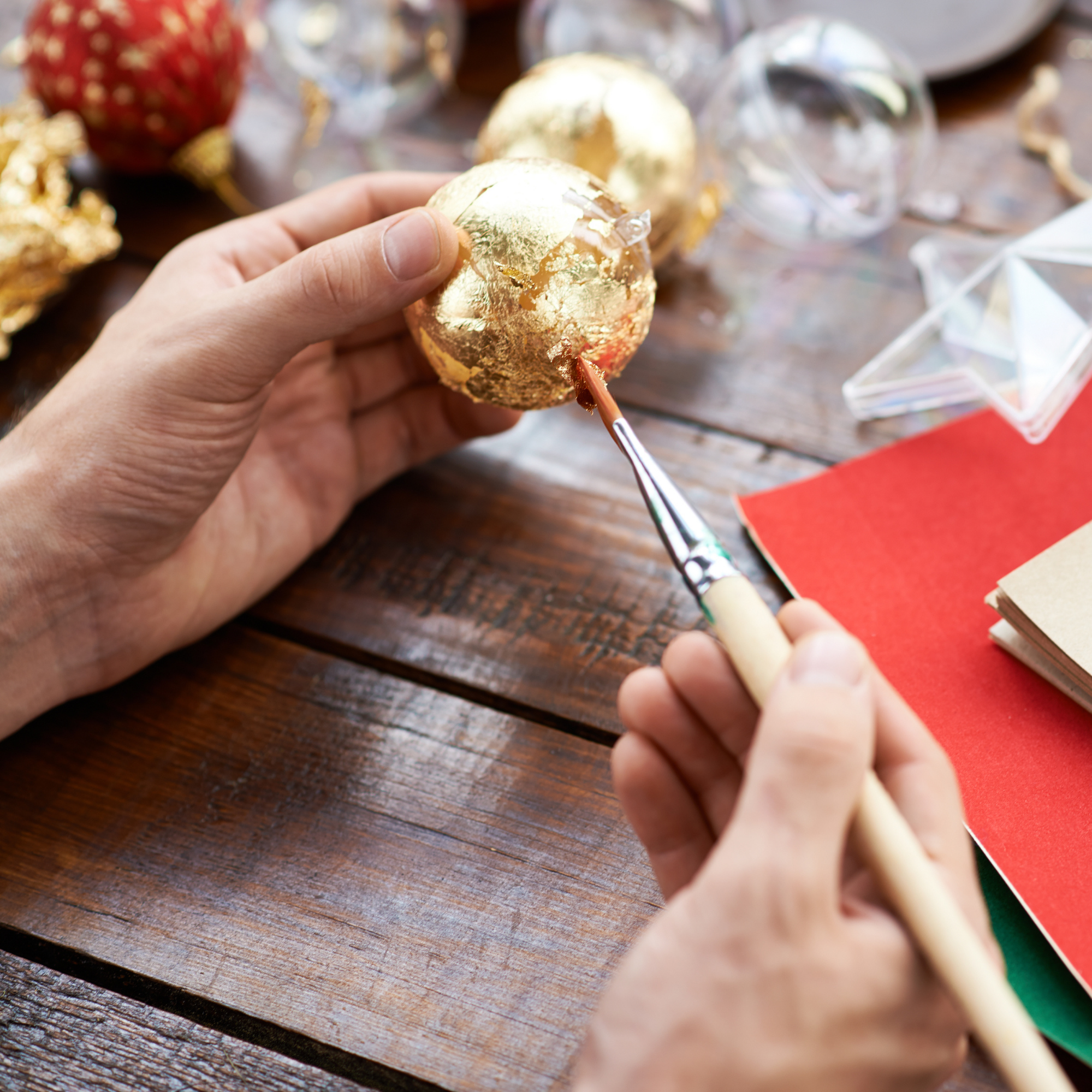 Photo showing hands applying gold foil to an ornament with other crafting materials in the background.