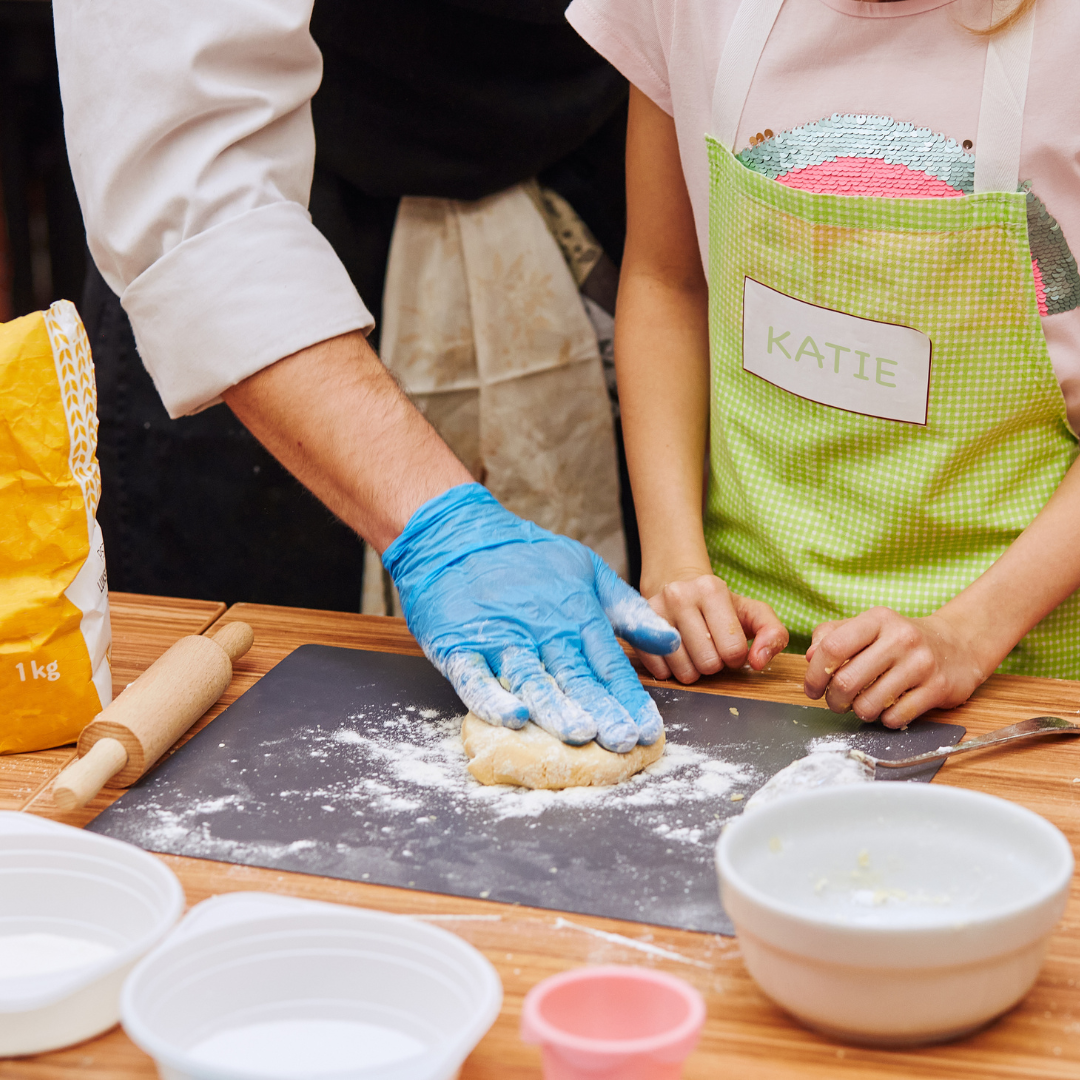 Photo of adult's hands assisting child's hands while working dough.