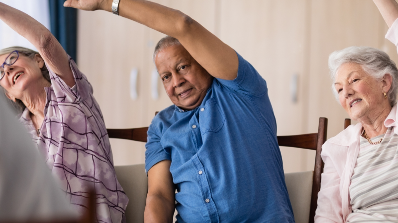 A group of older individuals completing chair exercises and stretches.