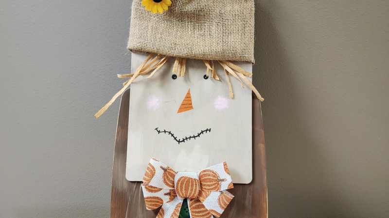 Photo of scarecrow made with two overlapping cutting boards and decorated with a Fall theme.